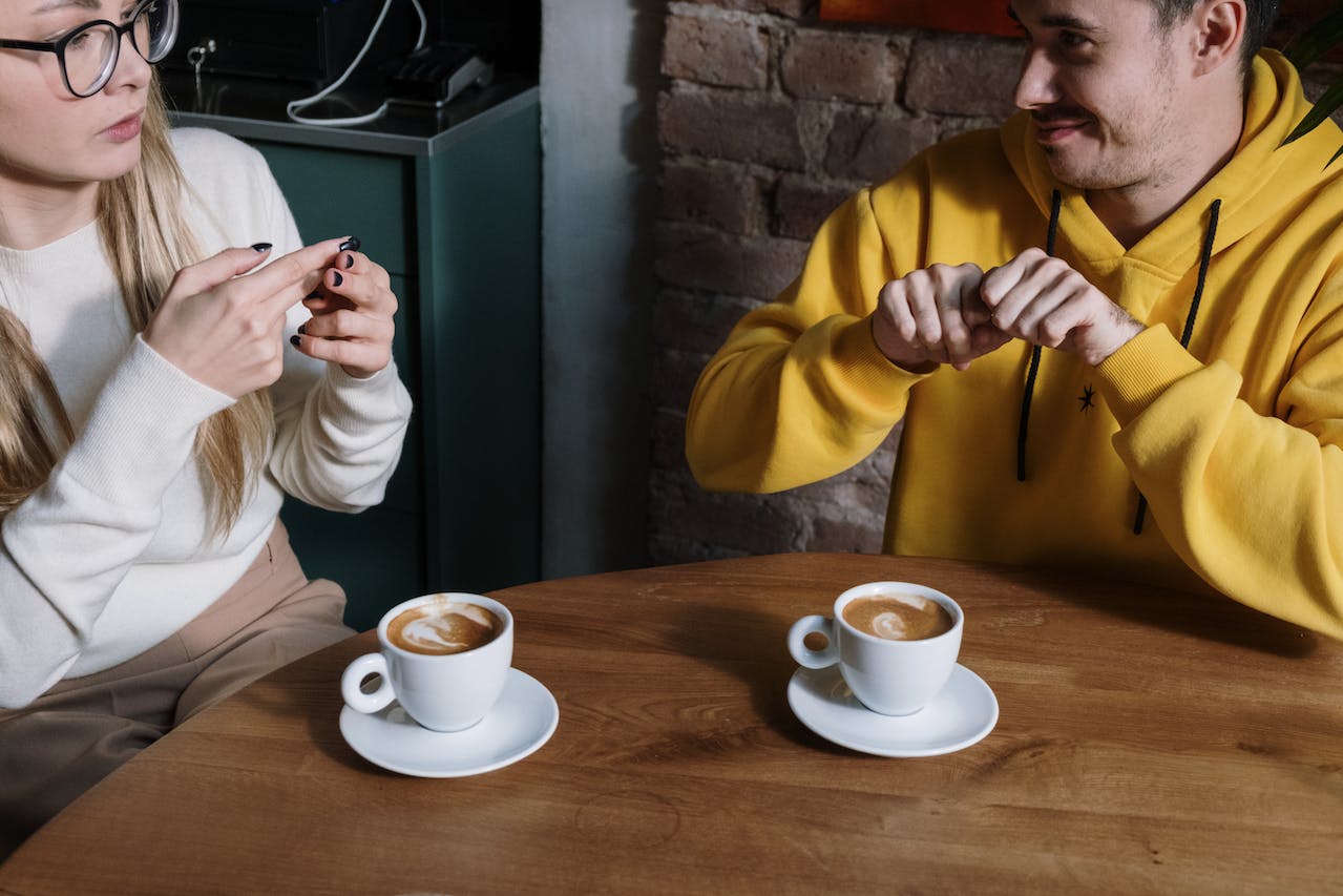 two people using sign language to communicate over a cup of coffee